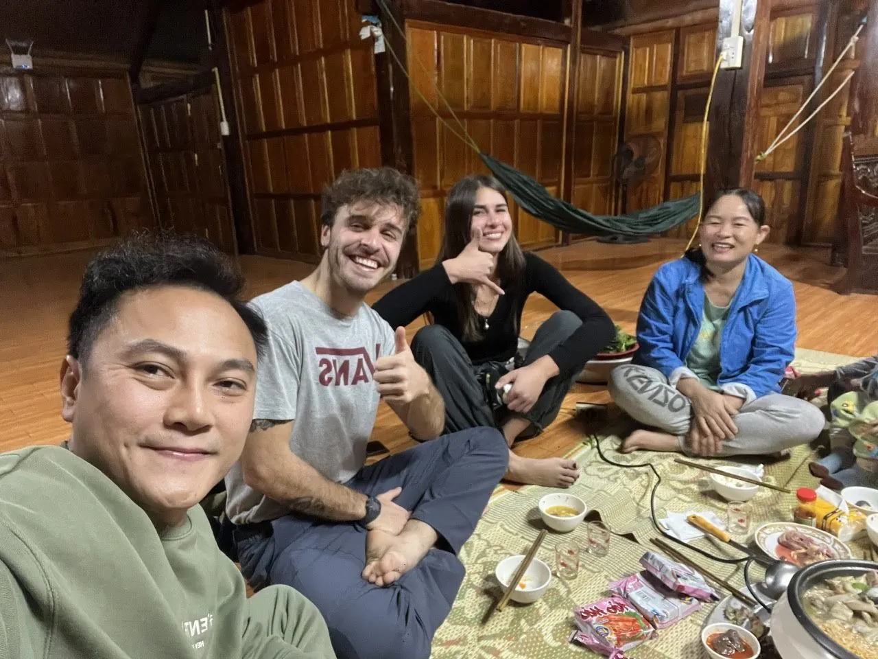 A group sharing dinner seated together on a woven mat on the floor of a homestay