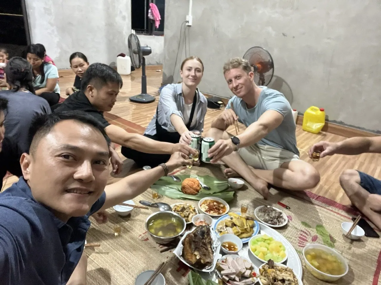 Travelers and their host raising a toast over a spread of home-cooked dishes at a homestay dinner